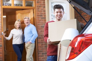Young man loads boxes into car as parents look on