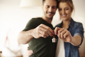 Young couple hug and hold miniature house towards camera