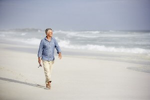 Older man walks along the beach holding a fishing rod