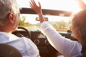 Older couple in convertible car, woman has her hands in the air