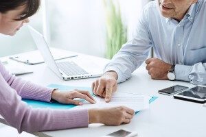 Two people sit opposite one another at a desk and look over a document